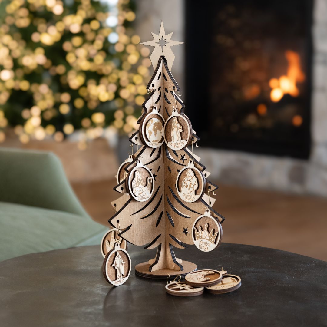 A wooden Christmas tree ornament display with carved profile figures and star details, set on a dark table in front of a blurred fireplace and festive lights.